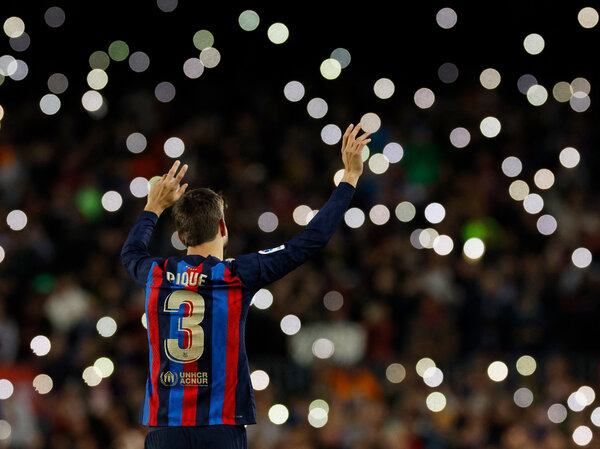 A picture of Piqué from his final game for Barcelona in November. He is wearing his No. 3 uniform with blue, red and black stripes and facing away from the camera. The lights in the stands are forming white circles.