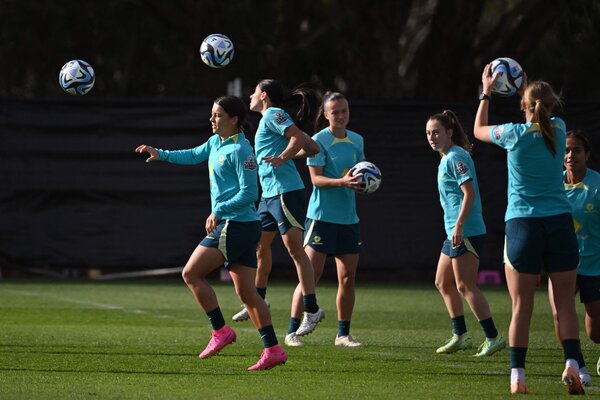 Sam Kerr, left, wearing pink cleats, is shown training with her Australian teammates. They’re all wearing light blue jerseys, and several have a soccer ball.